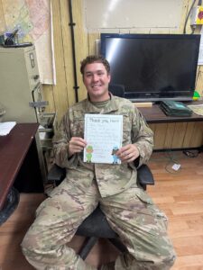 Deployed service members holding handwritten letters from supporters inside FSO care packages
