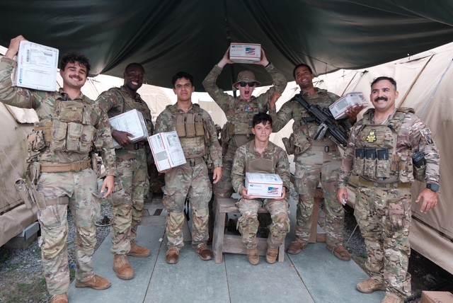 Deployed U.S. service members holding Forgotten Soldiers Outreach WE CARE packages received in June 2026.
